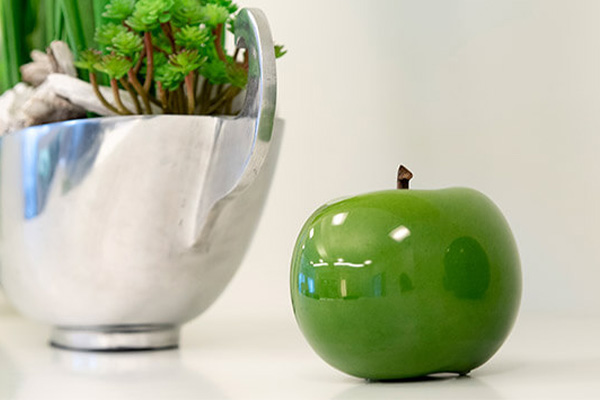 Grüner Apfel auf einem Tisch neben einem Blumentopf mit Blumen